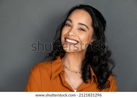 Photo of Close up face of young woman with beautiful smile isolated on grey wall with copy space. Successful multiethnic girl. Latin woman looking at camera against gray wall with a big whitening teeth smile.