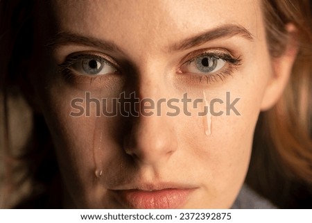 close up of the face of a young woman with tears running down her cheek.