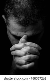Close up of faithful mature man praying, hands folded in worship to god with head down and eyes closed in religious fervor. Black background. Concept for religion, faith, prayer and spirituality. - Shutterstock ID 768357262