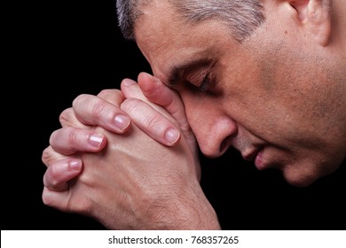 Close up of faithful mature man praying, hands folded in worship to god with head down and eyes closed in religious fervor. Black background. Concept for religion, faith, prayer and spirituality. - Shutterstock ID 768357265