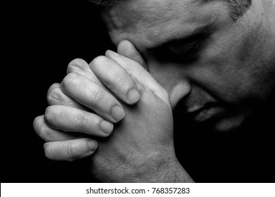 Close up of faithful mature man praying, hands folded in worship to god with head down and eyes closed in religious fervor. Black background. Concept for religion, faith, prayer and spirituality.