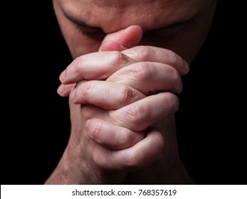 Close up of faithful mature man praying, hands folded in worship to god with head down and eyes closed in religious fervor. Black background. Concept for religion, faith, prayer and spirituality. - Shutterstock ID 768357619