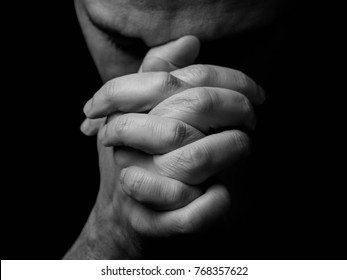 Close up de homem maduro fiel orando, mãos dobradas em adoração a Deus com a cabeça baixa e olhos fechados em fervor religioso. Fundo preto. Conceito para religião, fé, oração e espiritualidade.