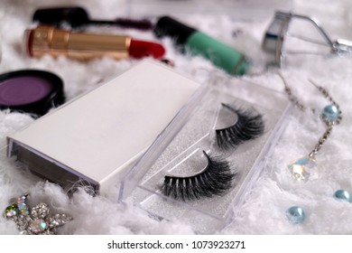 Close up of false eyelashes with make up tools and accessories such as brush on, lipstick, mascara and nail polish 