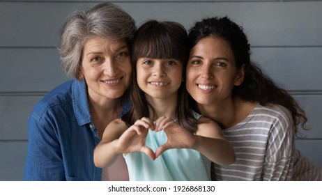 Close up family portrait of happy three generations of Hispanic women pose together show love heart hand gesture. Smiling little Latino girl child with young mother and senior grandmother feel united. - Shutterstock ID 1926868130