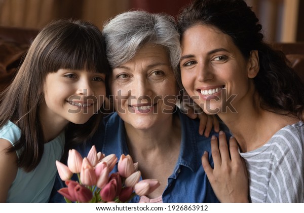 Close up family portrait of happy three generations
of Hispanic women pose together celebrating anniversary. Smiling
adult female with little daughter and mature grandmother on woman
day.