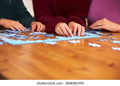 Close Up Of Family Sitting Around Table At Home Doing Jigsaw Puzzle Together