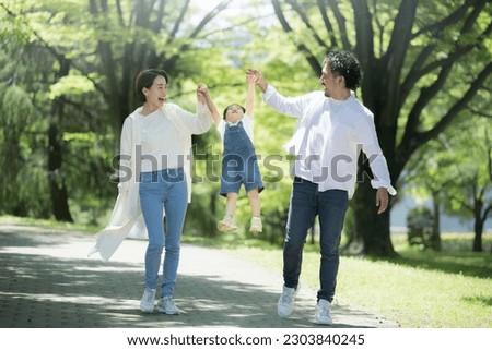 A close family strolling in the park Full-body, wide-angle image of a family with children jumping, holding hands in the fresh green 