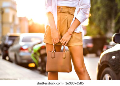 Close up fashion details of stylish woman wearing beige shorts holding luxury small bag, modern young businesswoman, sunny light on the Milano street. - Shutterstock ID 1638376585