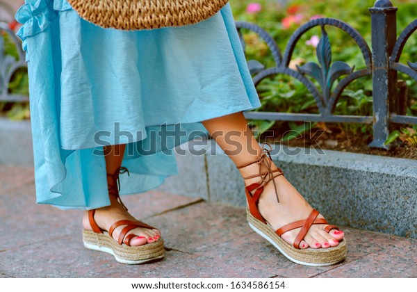 Close up\
fashion details of woman feet’s, elegant gladiator sandals, blue\
feminine dress, perfect for summer\
vacation.