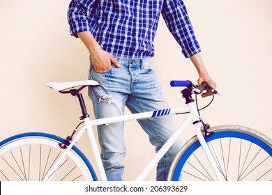 Close up fashion image of stylish guy in navy plaid shirt and vintage beans posing near beige background with his fix bike, not isolated. - Powered by Shutterstock