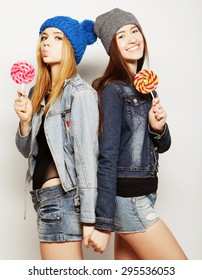 Close up fashion lifestyle portrait of two young hipster girls best friends, holding candys, making funny faces and have good time.