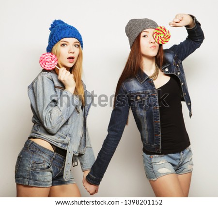 Close up fashion lifestyle portrait of two young hipster girls best friends, holding candys, making funny faces and have good time.