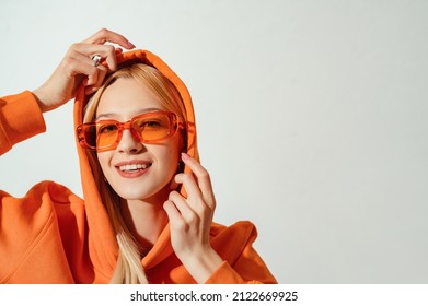 Close up fashion portrait of happy smiling blonde girl wearing trendy orange color glasses, oversized hoodie. Copy, empty space for text