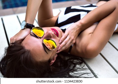 Close up fashion portrait of stunning tanned model relaxed near pool, tanned perfect skin, wearing crop top, mirrored sunglasses and watches, nature beauty, woman enjoy vacation. - Shutterstock ID 1134423830
