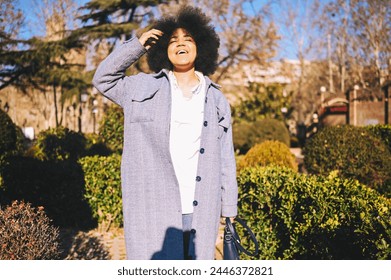 Close up Fashion street style portrait of attractive young natural beauty African American woman with afro hair in blue coat posing walking outdoors in sunny day. Happy lady with perfect teeth smile - Powered by Shutterstock