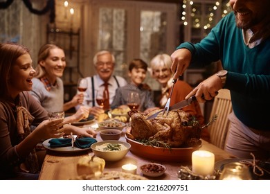 Close up of father carving Thanksgiving turkey during family meal at dining table.