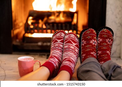 Close up of the feet of a Caucasian couple wearing slippers lying on the floor in front of a fire in their sitting room at Christmas time