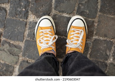 Close Up Feet Of Girl In Stylish Casual Shoes. Female In Yellow Sneaker Being Walking Down The Street. Woman Legs In In Shoes Walking On Sidewalk. 