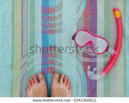Close up of feet on a patterned towel with basic snorkeling equipment - mask and snorkel