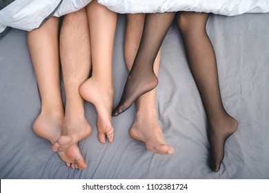 Close up feet of trio making love in bedroom. Sex party concept.