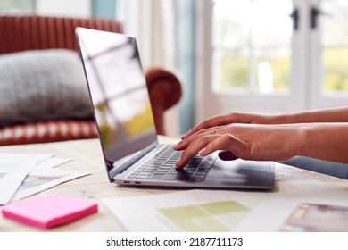 Close Up Of Female Architect Or Interior Designer Working From Home Looking At Designs On Laptop