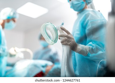 Cierre del brazo femenino en guantes estériles preparando equipos respiratorios para el paciente durante la cirugía. Señora con máscara protectora y vestido azul