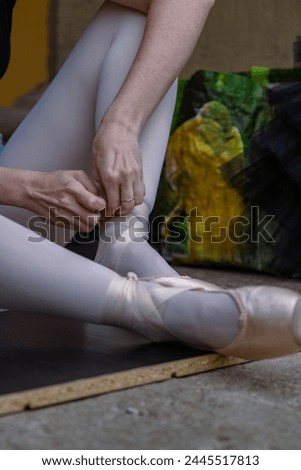 Close up of female ballet dancer putting on, tying ballet shoes. Adult ballerina sits on floor at dance studio and puts on pointe shoes before choreography lesson. Preparing to performance. 