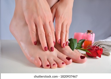 Close up of female bare feet and hands with red nails polish color in a salon and decoration on the desk in the background. Pedicure and manicure concept