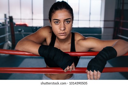 Close up of a female boxer standing inside a boxing ring. Boxer resting her arms on the rope of boxing ring. - Powered by Shutterstock