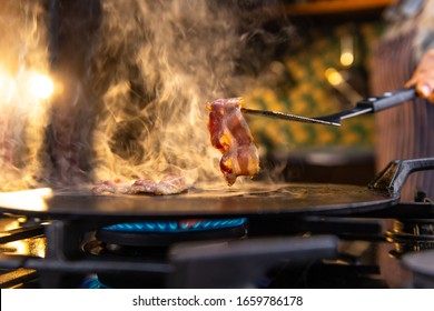 Close up of a female chef flipping a sizzling, hot pieces of bacon on a kitchen stove. 
