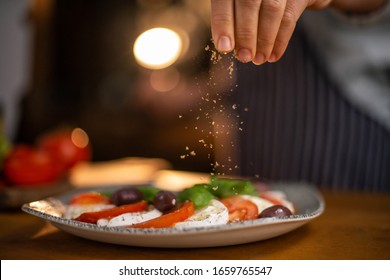 Close up of female chef hands seasoning a plate of freshly made tomato and mozzarella salad. 