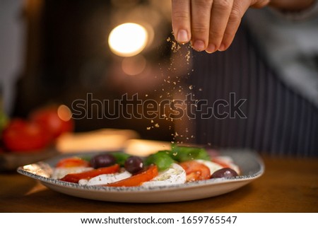 Close up of female chef hands seasoning a plate of freshly made tomato and mozzarella salad. 