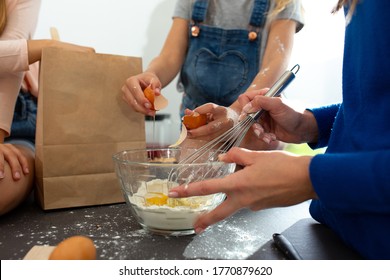 Close Up Of Female Child Hands Cracking Egg Into Bowl While Young Woman Mixing Ingredients With Whisk