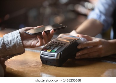 Close up of female client hold smartphone paying for order using modern easy nfc technology, waiter give card reader machine for customer make payment transaction with cashless contactless method