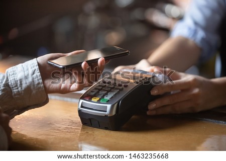 Close up of female client hold smartphone paying for order using modern easy nfc technology, waiter give card reader machine for customer make payment transaction with cashless contactless method