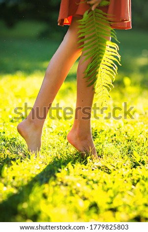 Close up female crossed legs walking on the grass,orange dress  green grass and fern.