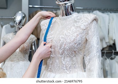 close up of female designer dressmaker hand fitting bridal dress with measure tape in  boutique