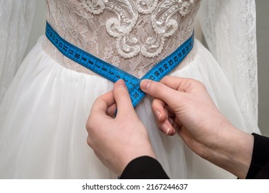 Close Up Of Female Designer Dressmaker Hand Fitting Bridal Dress With Measure Tape In  Boutique