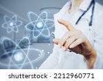 Close up of female doctor hand pointing at abstract glowing atom hologram on blurry hospital or clinic interior background. Nuclear medicine, energy and medical research concept