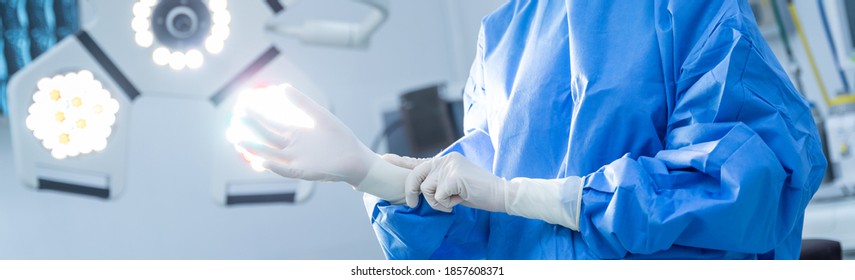 Close Up Of Female Doctor Hands With Surgical Gloves In The Operating Room. Medical Staff Protective Gear Against Coronavirus COVID 19. Health Care, Hospital Safety Concept Style Banner Background