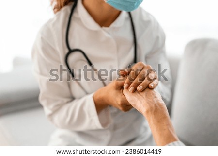 Close up of female doctor in lab coat with stethoscope holding hands with senior patient. Female doctor and patient holding hands as a way of support.