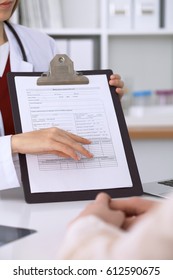 Close up of a female doctor pointing into an application form while consulting patient. Medicine and health care concept