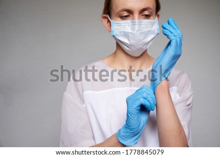 Close up of female doctor or scientist in protective medical mask over grey background. She is puting on gloves
