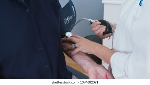 Close Up Of Female Doctor Taking Blood Pressure With Bp Cuff On Senior Patient. Older Caucasian Woman Having Her Vitals Taken During Regular Check Up With Physician