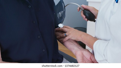 Close Up Of Female Doctor Taking Blood Pressure With Bp Cuff On Senior Patient. Older Caucasian Woman Having Her Vitals Taken During Regular Check Up With Physician