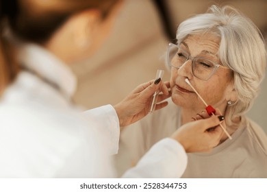 Close up of female doctor taking sample with cotton swab from sick senior woman's nose. Home doctor's visit. - Powered by Shutterstock