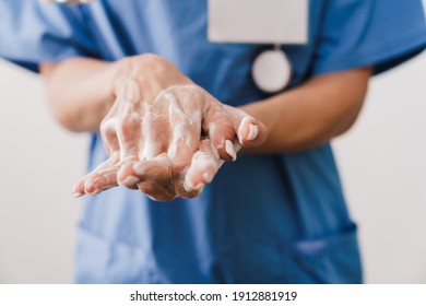 Close up of a female doctor washing her hands with soap isolated over white background - Shutterstock ID 1912881919