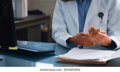 Close Up Of Female Doctor Wearing White Coat Sitting Behind Desk In Office Reviewing Patient Notes - Powered by Shutterstock