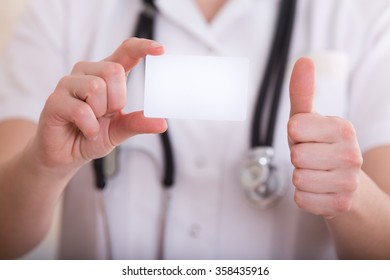 Close Up Of Female Doctor's Hand Showing Blank Business Card And Thumb Up. Health Care Concept